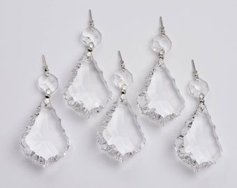 May include: Six clear crystal chandelier pendants with a teardrop shape and faceted edges. Each pendant is connected to a smaller, round crystal bead with a silver-colored metal pin. The pendants are arranged against a white background.