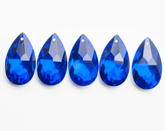 May include: Five teardrop-shaped crystal prisms in a vibrant blue color. The prisms are arranged in a row on a white background.