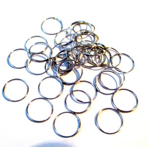 May include: A pile of silver jump rings, a type of metal ring used for jewelry making and crafting.