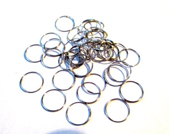 May include: A pile of silver jump rings, a type of metal ring used for jewelry making and crafting.