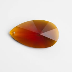 May include: A teardrop-shaped crystal prism with a red and orange gradient. The prism has a small hole at the top for hanging.