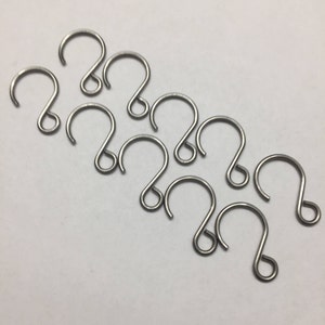 May include: Ten silver-toned metal hooks with a rounded shape. The hooks are arranged in a semi-circle pattern on a white surface.