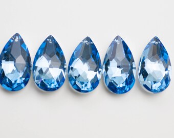 May include: Five teardrop-shaped crystal pendants in a light blue color. The pendants are arranged in a row on a white background.
