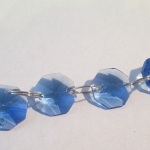 May include: A strand of light blue crystal beads connected by silver jump rings. The beads are faceted and have a slightly iridescent sheen.