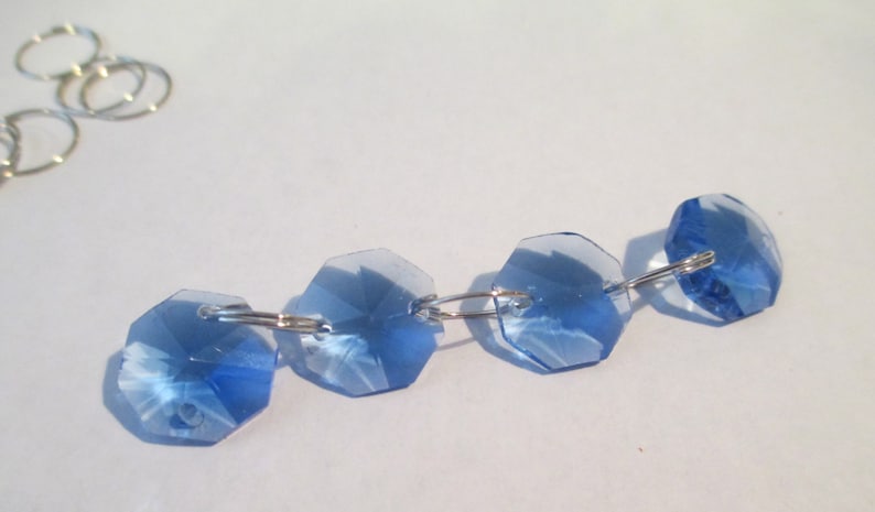 May include: A strand of light blue crystal beads connected by silver jump rings. The beads are faceted and have a slightly iridescent sheen.