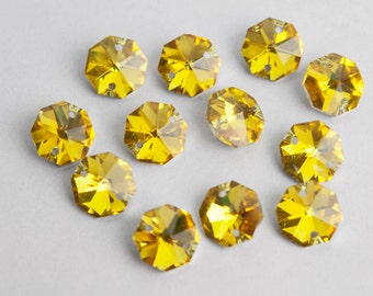 May include: A collection of 12 yellow faceted glass rhinestones with a hole in the center. The rhinestones are arranged in a heart shape on a white background.