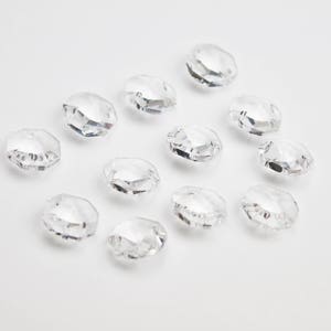 May include: A collection of clear crystal faceted beads, arranged in a semi-circle pattern on a white background. The beads are all the same size and shape, and they have a shiny, reflective surface.
