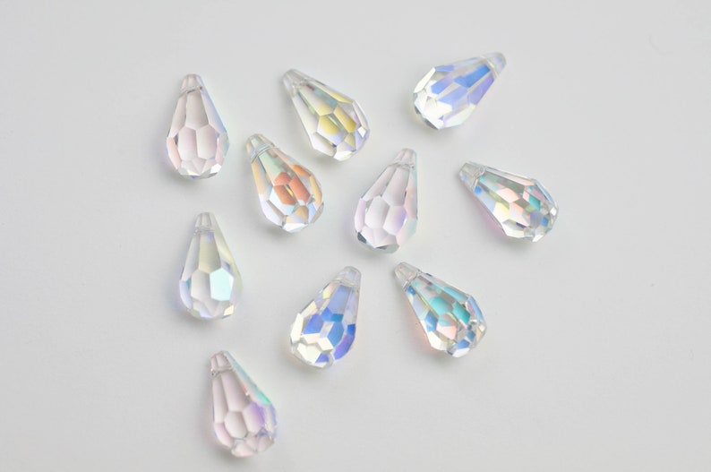 May include: A collection of iridescent teardrop-shaped crystal beads. The beads are clear with a rainbow sheen.