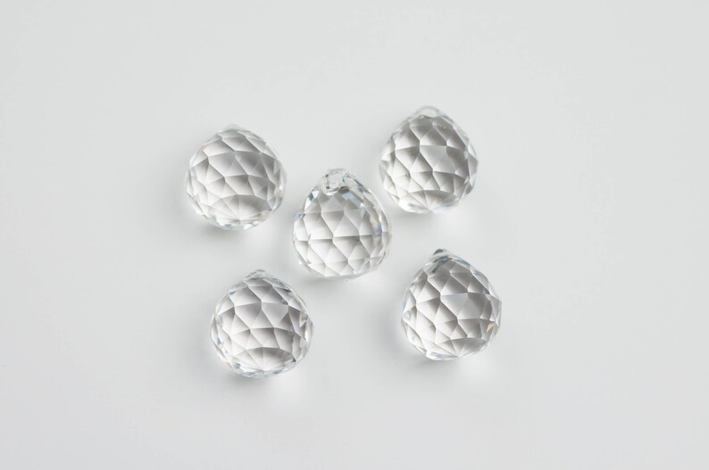 May include: Five clear crystal prisms, each with a faceted design, are arranged on a white surface.