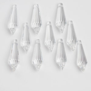 May include: Ten clear crystal teardrop-shaped pendants with faceted edges. The pendants are arranged in a staggered pattern on a white background.
