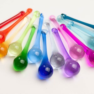 May include: A rainbow assortment of teardrop-shaped glass ornaments. The ornaments are arranged in a semi-circle, with the colors transitioning from red to purple.