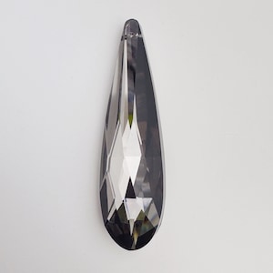 May include: A teardrop-shaped crystal pendant with a faceted design. The crystal is clear with a dark gray hue.