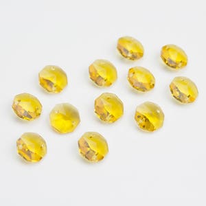 May include: A collection of 12 amber-colored faceted crystal beads. The beads are round and have a smooth, polished finish.