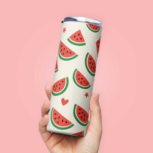 Può includere: Un bicchiere in acciaio inossidabile bianco con un motivo ripetuto di fette di anguria rosse su sfondo bianco. Il bicchiere ha un coperchio argentato.