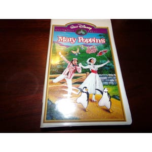 Op de afbeelding: Een VHS-band van de film "Mary Poppins" uit de Walt Disney Masterpiece Collection. De hoes toont illustraties van Mary Poppins, Bert en dansende pinguïns. De titel staat in een decoratief lettertype met een gouden rand.