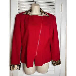 May include: A red jacket with a diagonal zipper closure and a leopard print collar and cuffs. The jacket is displayed on a mannequin against a white background. The jacket has long sleeves.