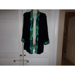 May include: Black open-front jacket with a colorful abstract pattern in shades of teal, green, and blue along the lapels and cuffs. The jacket is displayed on a mannequin against a white background.