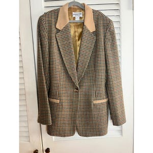 Op de afbeelding: Een Pendleton blazer in een ruitpatroon met bruine, groene en rode tinten. De blazer heeft een beige kraag en zakafwerking, met een enkele knoopsluiting. De binnenvoering is goudkleurig.