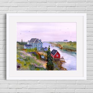 May include: Watercolor painting of a coastal scene with a red building and a blue building. The painting is framed in a white border and depicts a river, buildings, and a cloudy sky. The artwork is displayed on a white brick wall.
