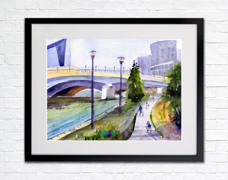 May include: Watercolor painting of a bridge over a river with people walking and biking on a path along the riverbank. The bridge is made of concrete and has a light blue railing. There are trees and buildings in the background.