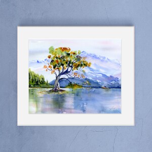 May include: Watercolour painting of a solitary tree with yellow and green leaves standing in a lake with mountains in the background.