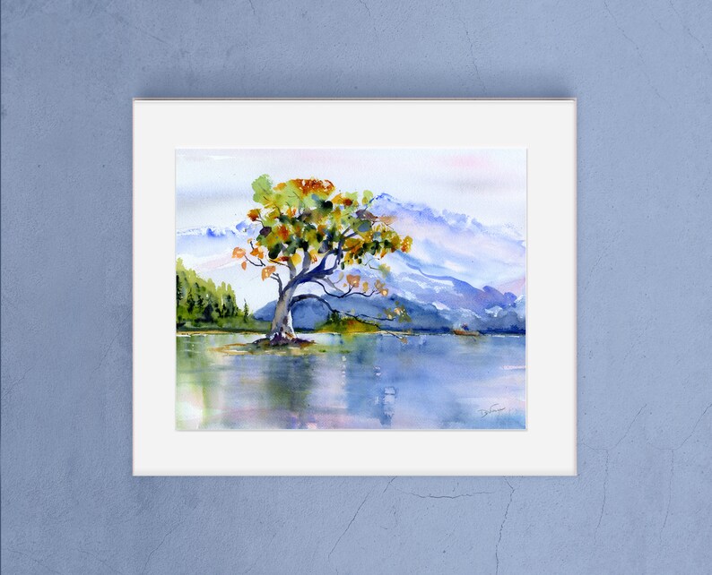 May include: Watercolour painting of a solitary tree with yellow and green leaves standing in a lake with mountains in the background.