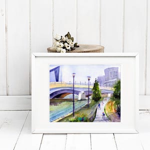 May include: A watercolor painting of a bridge over a river with buildings in the background. The bridge is yellow and has arches. There are trees and people walking on the path next to the river.
