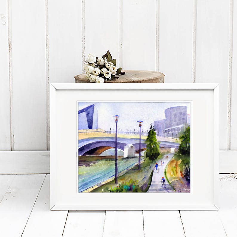 May include: A watercolor painting of a bridge over a river with buildings in the background. The bridge is yellow and has arches. There are trees and people walking on the path next to the river.