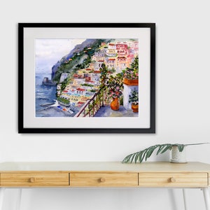 May include: A watercolor painting of a colorful Italian village on a cliffside overlooking the sea. The painting features a balcony with potted plants and a view of the ocean.