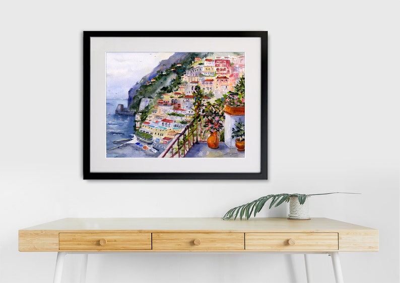 May include: A watercolor painting of a colorful Italian village on a cliffside overlooking the sea. The painting features a balcony with potted plants and a view of the ocean.