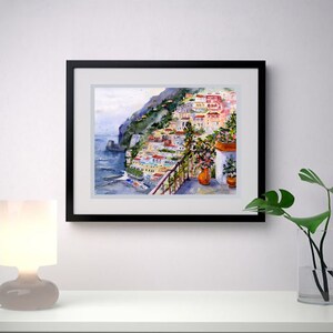 May include: Watercolor painting of a colorful Italian village on a cliffside overlooking the sea. The painting features a balcony with potted plants and a view of the ocean.