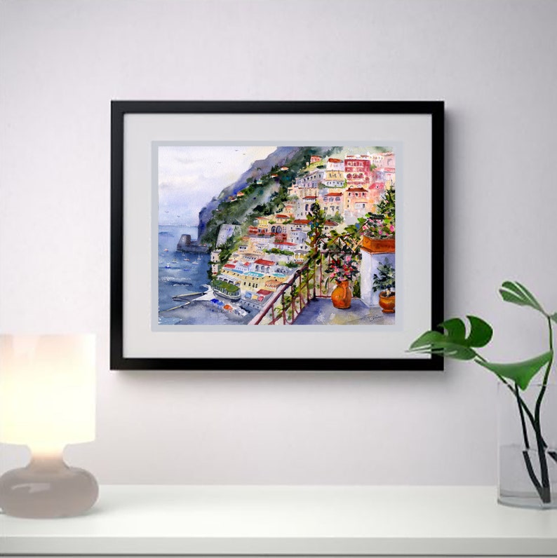 May include: Watercolor painting of a colorful Italian village on a cliffside overlooking the sea. The painting features a balcony with potted plants and a view of the ocean.