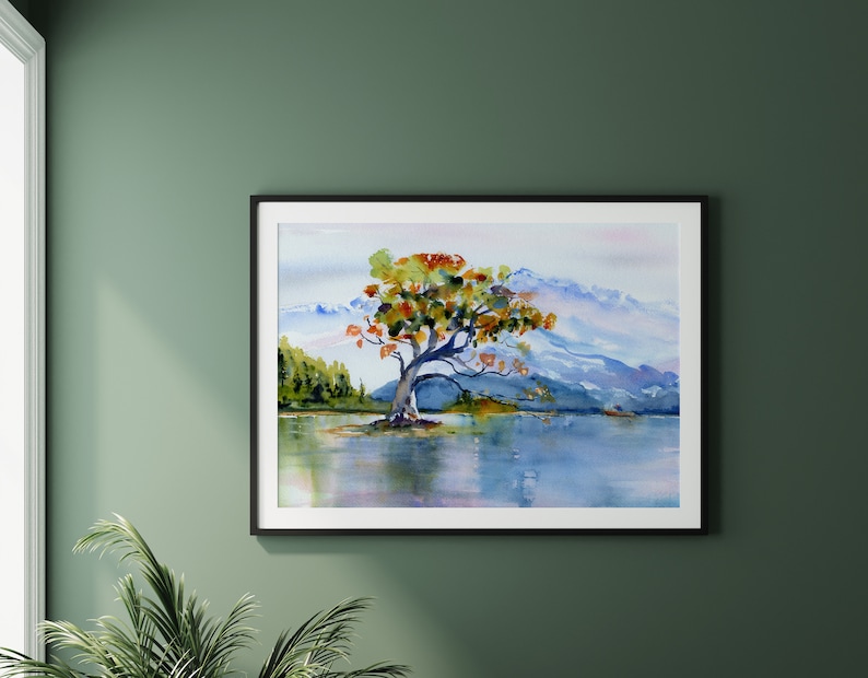 May include: Watercolour painting of a solitary tree with orange, yellow, and green leaves standing in a lake with mountains in the background.