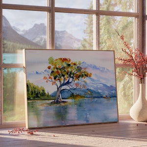 May include: A framed watercolour painting of a solitary tree with orange and yellow leaves in a mountainous landscape. The tree is in the foreground, with the mountains in the background. The water is a pale blue colour, and the sky is a light grey colour.