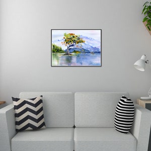 May include: Watercolour painting of a solitary tree with orange and green leaves on a small island in a lake. The lake is surrounded by mountains and a blue sky.