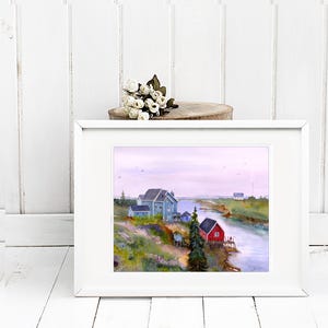 May include: A framed watercolor painting depicts a coastal scene with blue houses, a red building, and a river. The artwork is set in a white frame, with a small bouquet of white flowers on a wooden slice above it.