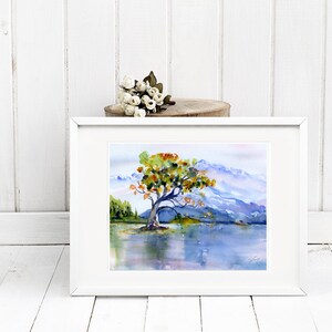 May include: A framed watercolour painting of a solitary tree with orange and yellow leaves standing in a lake with mountains in the background.