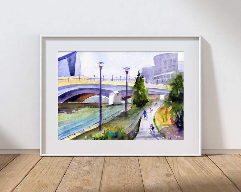 May include: Watercolor painting of a bridge over a river with people walking and biking on a path along the riverbank. The painting features a modern building in the background and streetlights along the path.