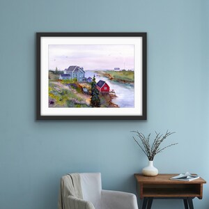 May include: Watercolor painting of a coastal scene with a river, houses, and a red building. The artwork is framed in a black frame and hangs on a light blue wall. The painting depicts a serene landscape with a focus on the natural beauty of the area.