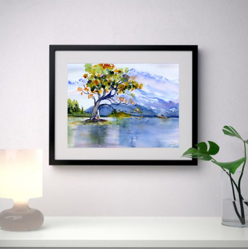 May include: Watercolour painting of a solitary tree with yellow and green leaves standing in a lake with mountains in the background.