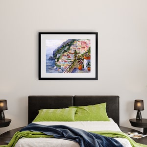 May include: A watercolor painting of a colorful Italian village on a cliffside overlooking the sea. The painting is framed in black and hangs on a white wall.