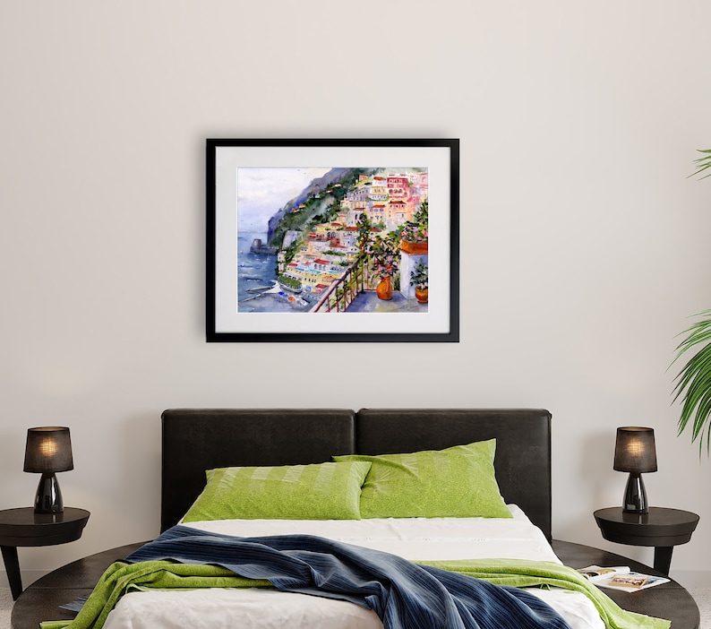 May include: A watercolor painting of a colorful Italian village on a cliffside overlooking the sea. The painting is framed in black and hangs on a white wall.