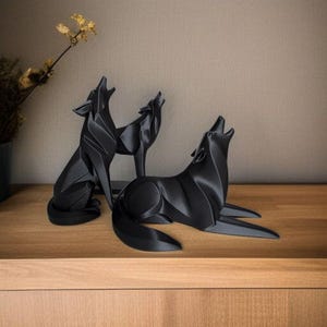 May include: Three black wolf sculptures in various poses, howling with their mouths open. The sculptures are on a wooden surface, with a neutral background. The wolves have a modern, geometric design.