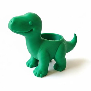 May include: A bright green dinosaur-shaped planter with a smiling face. The planter has a round opening on its back for plants and a curved tail. The dinosaur is standing on four legs.