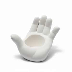 May include: A white ceramic hand-shaped decorative bowl. The bowl is open at the palm, with fingers extended. The object is a solid white color and sits on a white background.
