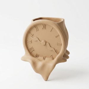 Puede incluir: Una escultura de reloj surrealista de color beige con números romanos. La esfera del reloj parece estar derritiéndose, con la parte inferior fluyendo hacia abajo. La escultura tiene una abertura en forma de jarrón en la parte superior.