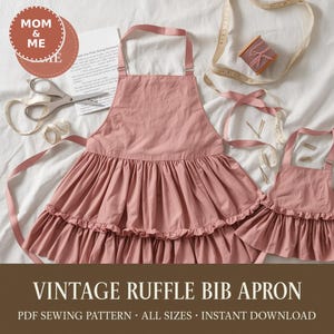 May include: A vintage ruffle bib apron in a dusty rose color, with a matching smaller apron. The aprons have a ruffled skirt and adjustable straps. The image also includes scissors, ribbon, and the text "MOM & ME" and "VINTAGE RUFFLE BIB APRON".