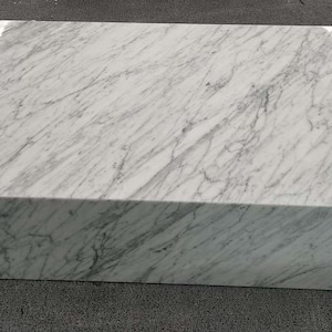 May include: A large, white marble coffee table with a rectangular top and a thick base. The table has a smooth, polished surface with a subtle veining pattern.