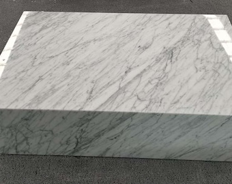 May include: A large, white marble coffee table with a rectangular top and a thick base. The table has a smooth, polished surface with a subtle veining pattern.