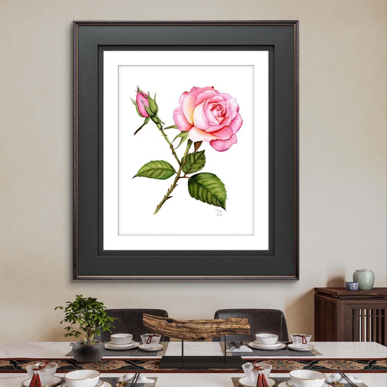 A hand-painted watercolor of a rose in full bloom, featuring soft shades of pink with detailed shading and texture that bring the delicate petals to life displayed in a sleek black frame, providing a bold contrast to the soft colors of the watercolor
